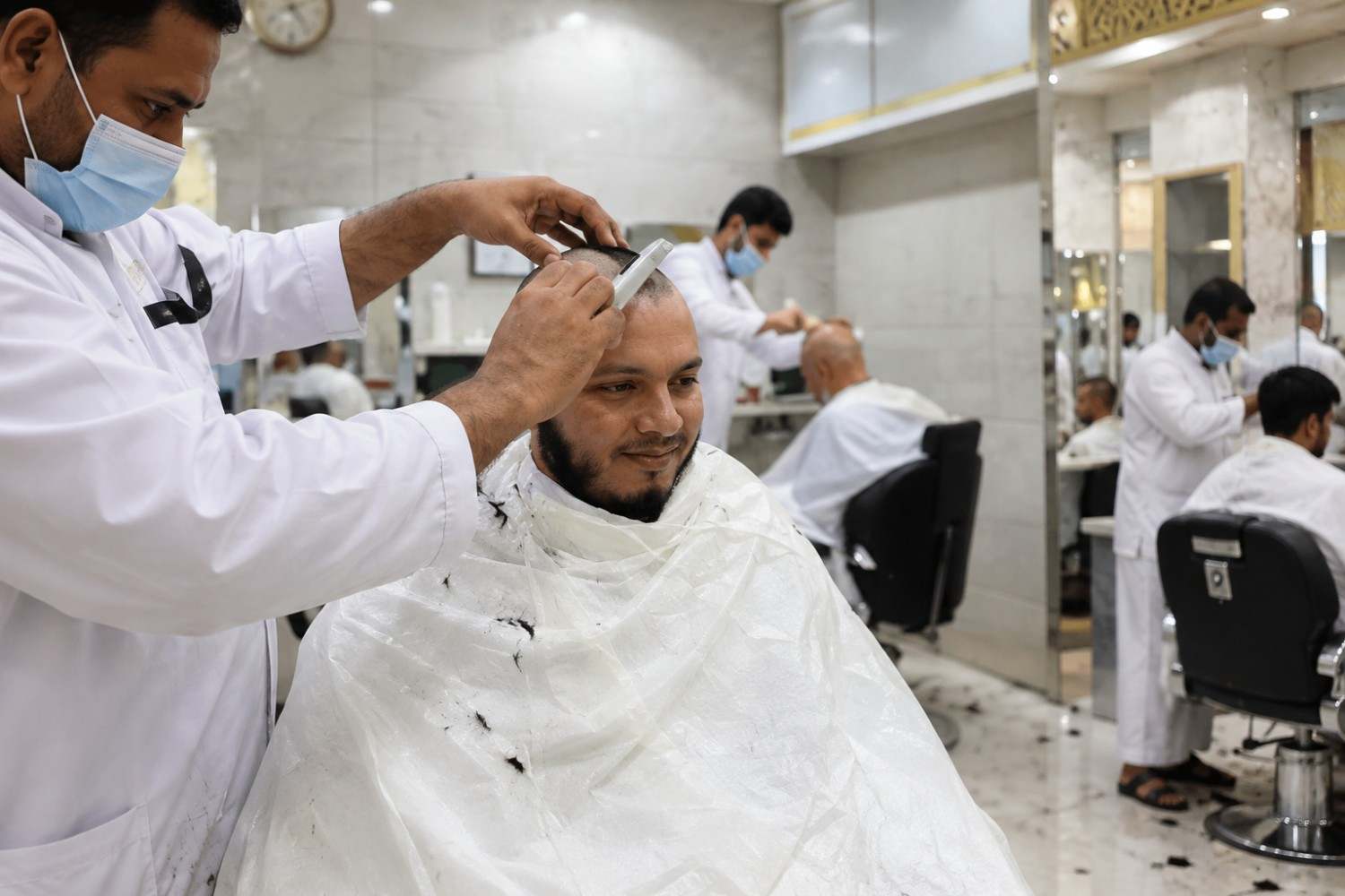 A barber shaving a pilgrim's head at a licensed barbershop near the Haram after Umrah